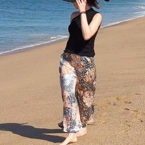 Woman strolling on a beach while modeling LYC Palazzo Pants in Tropical Silk Spanish Rose.